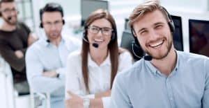 Smiling team of professionals wearing a headset and facing camera at their desk