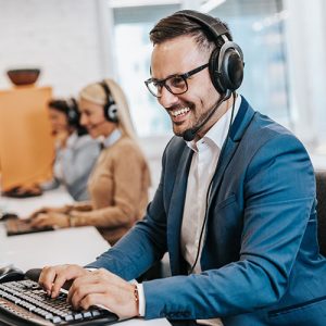Smiling man in business attire wearing headphones and working on a desktop computer