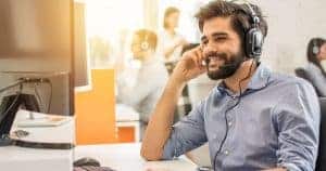 Smiling customer support man wearing a headphone at a white desk